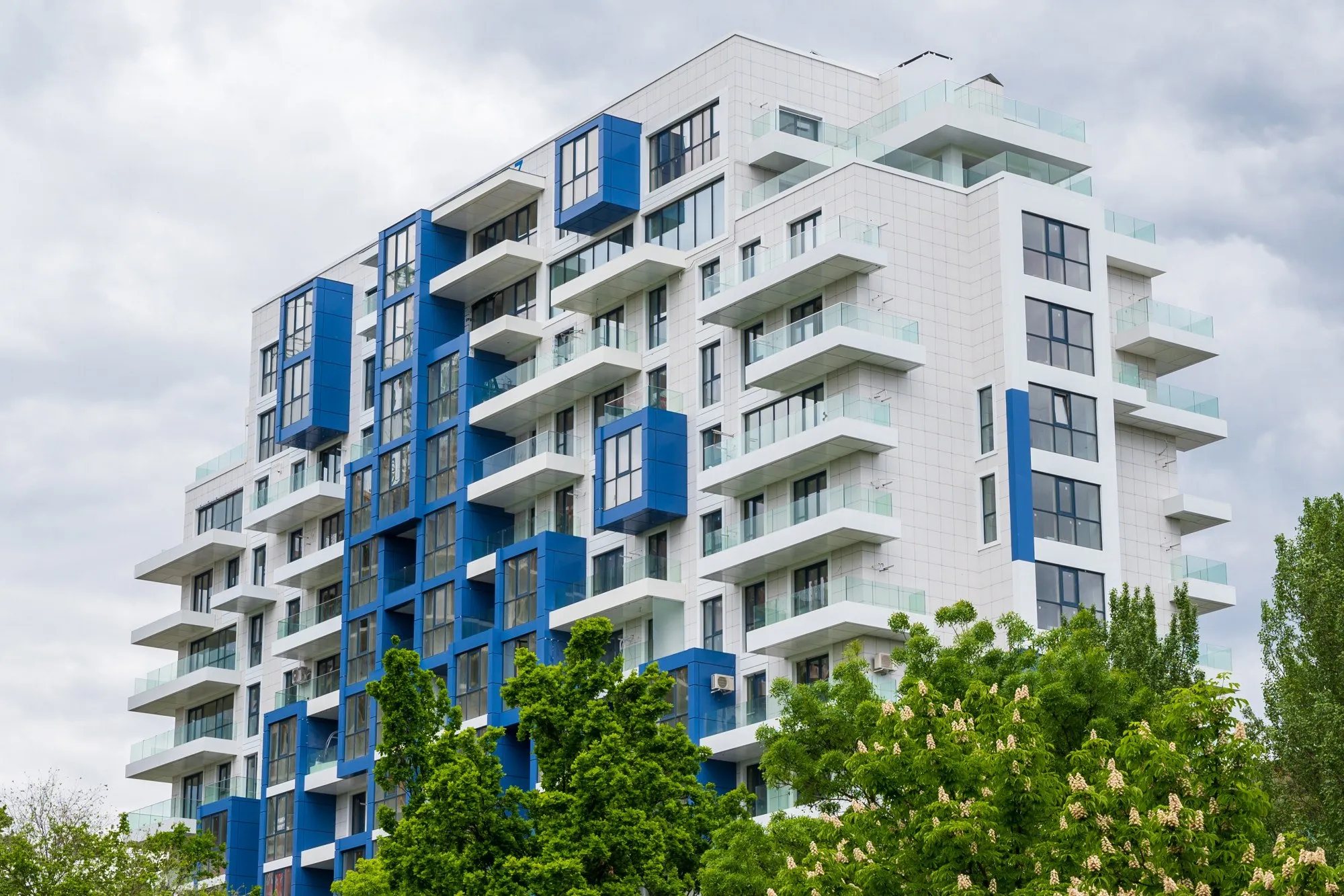 White apartment tower with bright blue balcony panels above trees