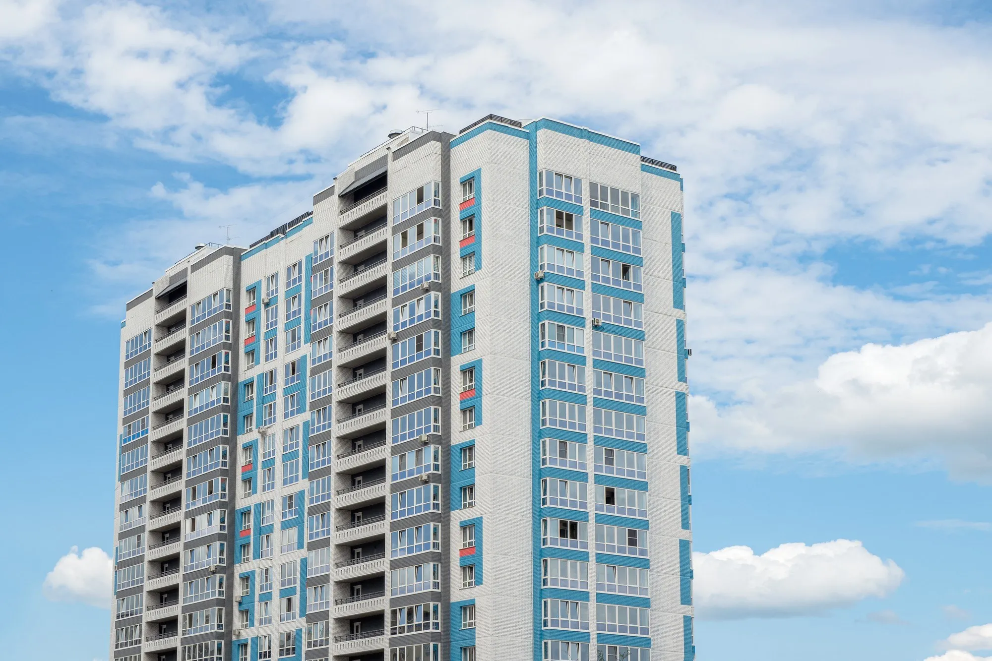 Tall white residential tower with blue window frames against a clear sky